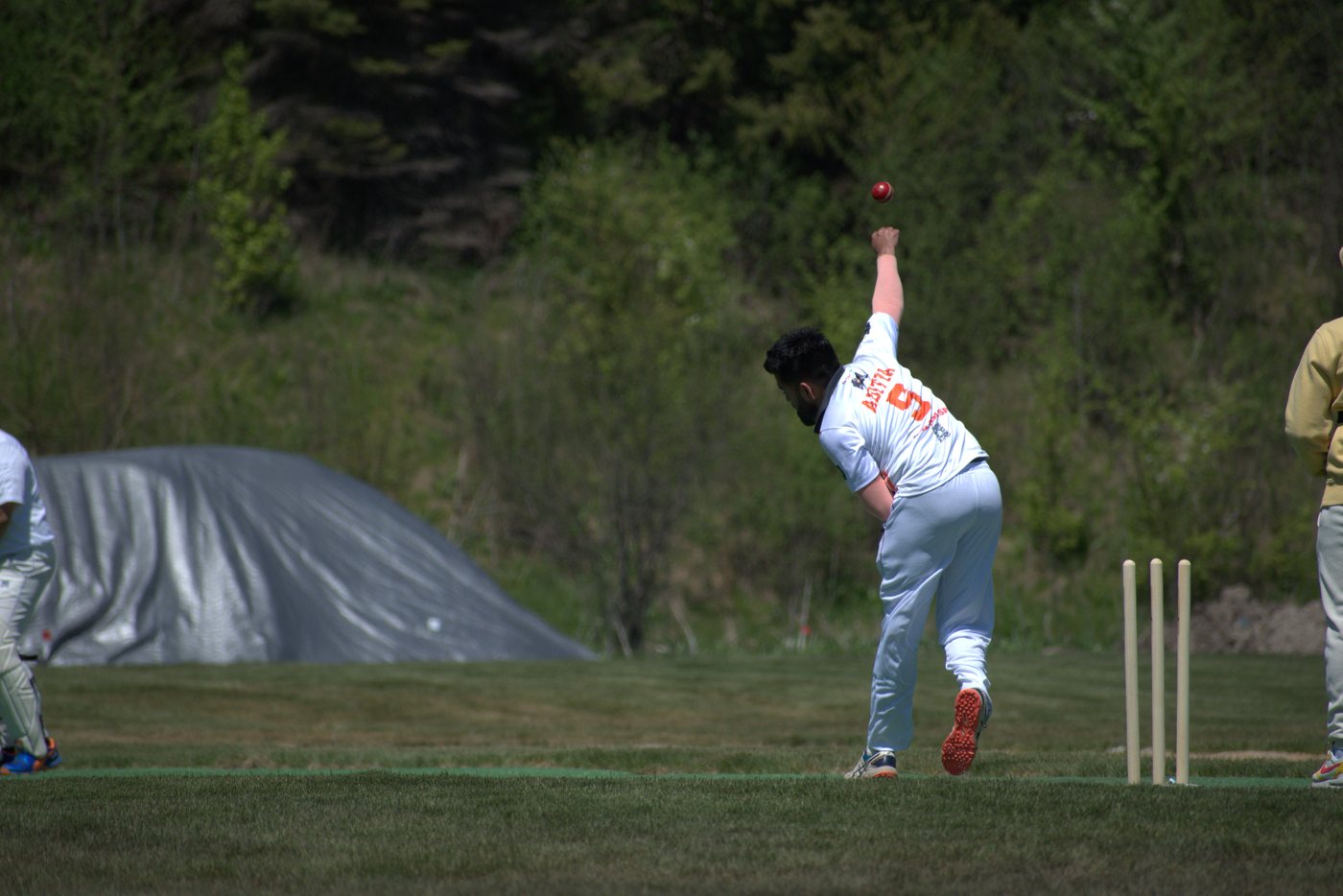 Aditya at full stretch in delivery, the red ball frozen above his hand